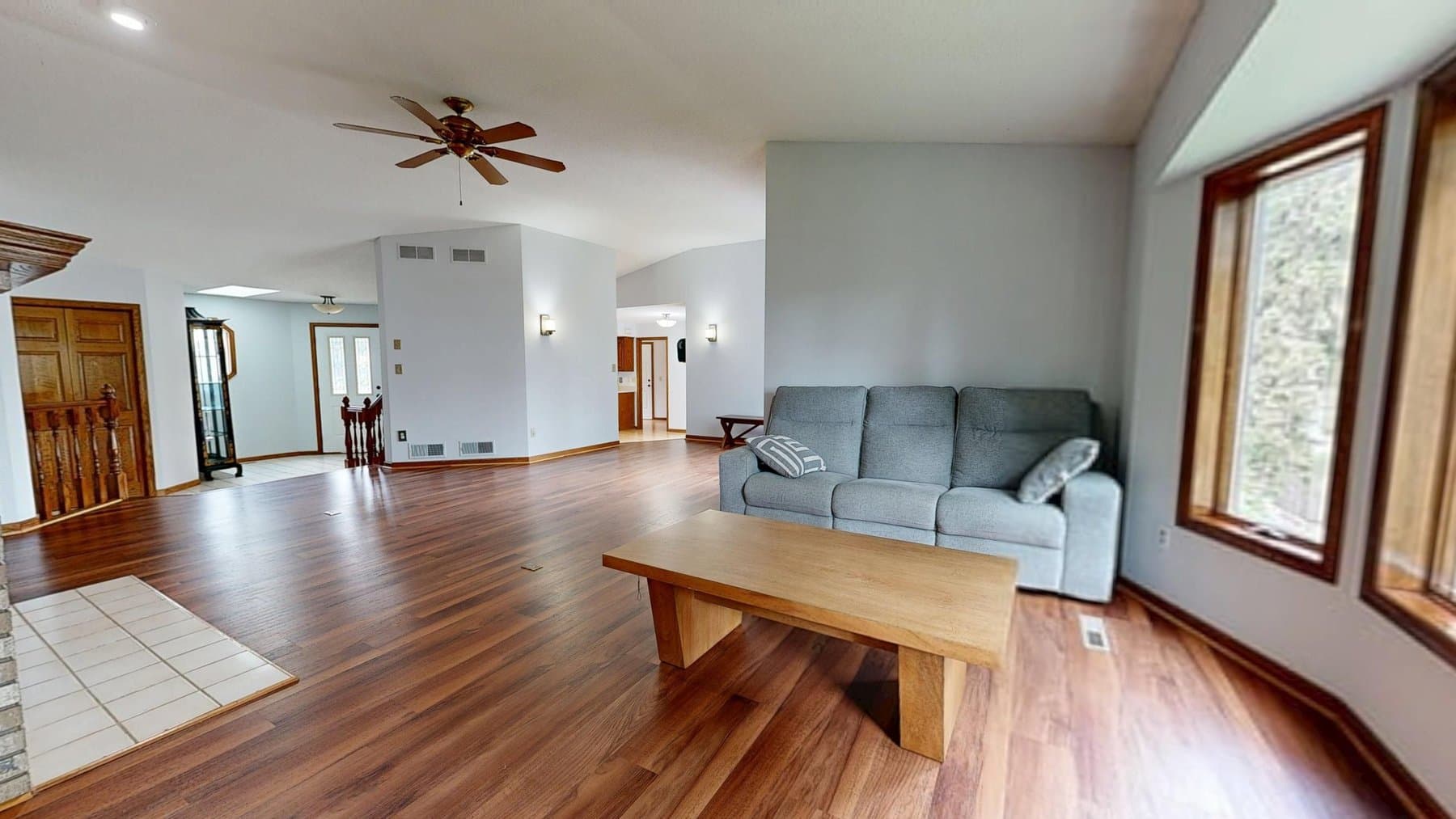 A bright, open-plan living room with warm hardwood floors and neutral staging