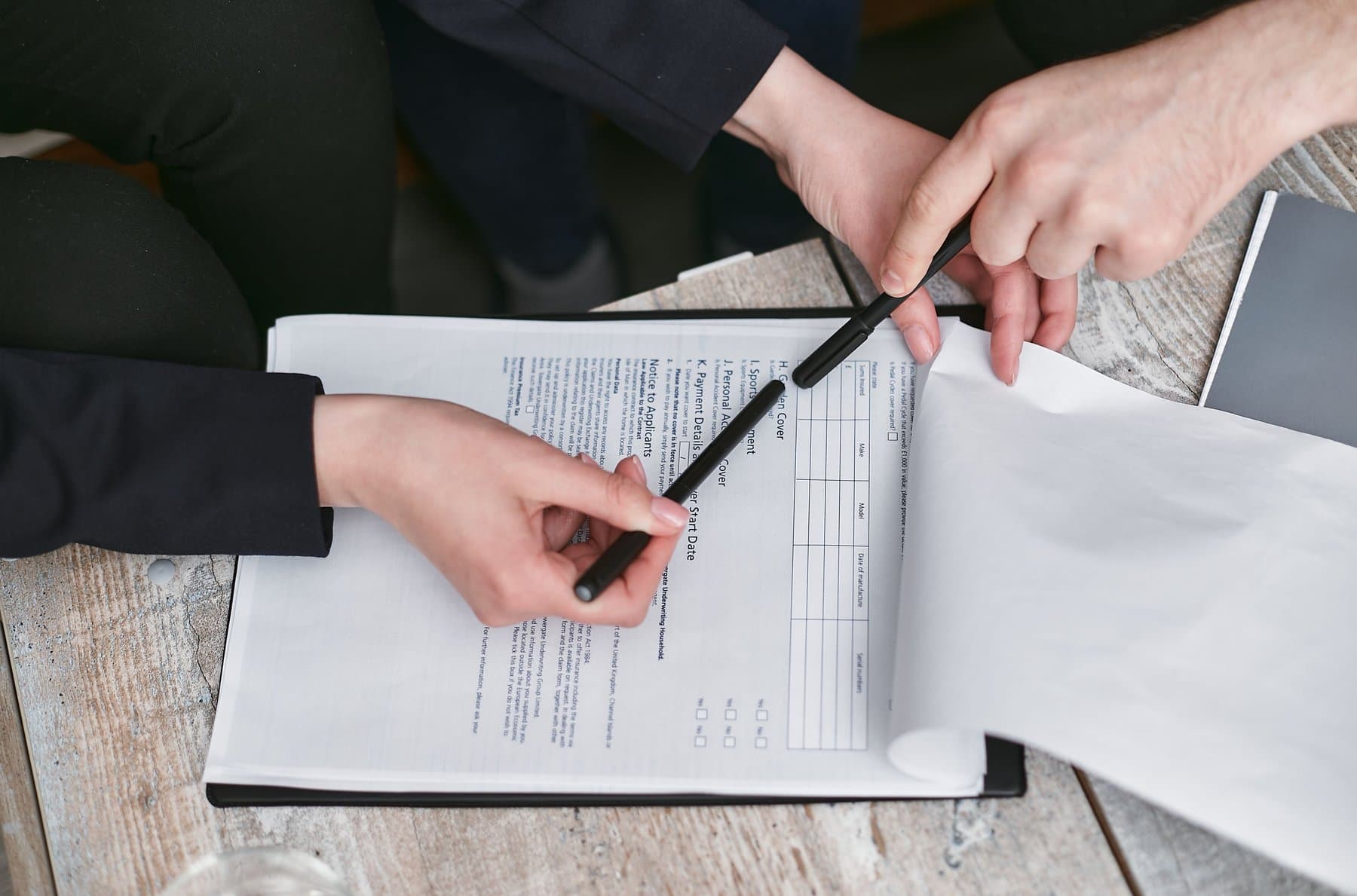 A hand holding a pen while reviewing a contract on a warm wood table
