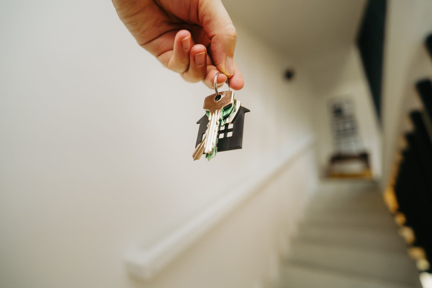 A hand holding a house-shaped keychain in a softly lit stairwell