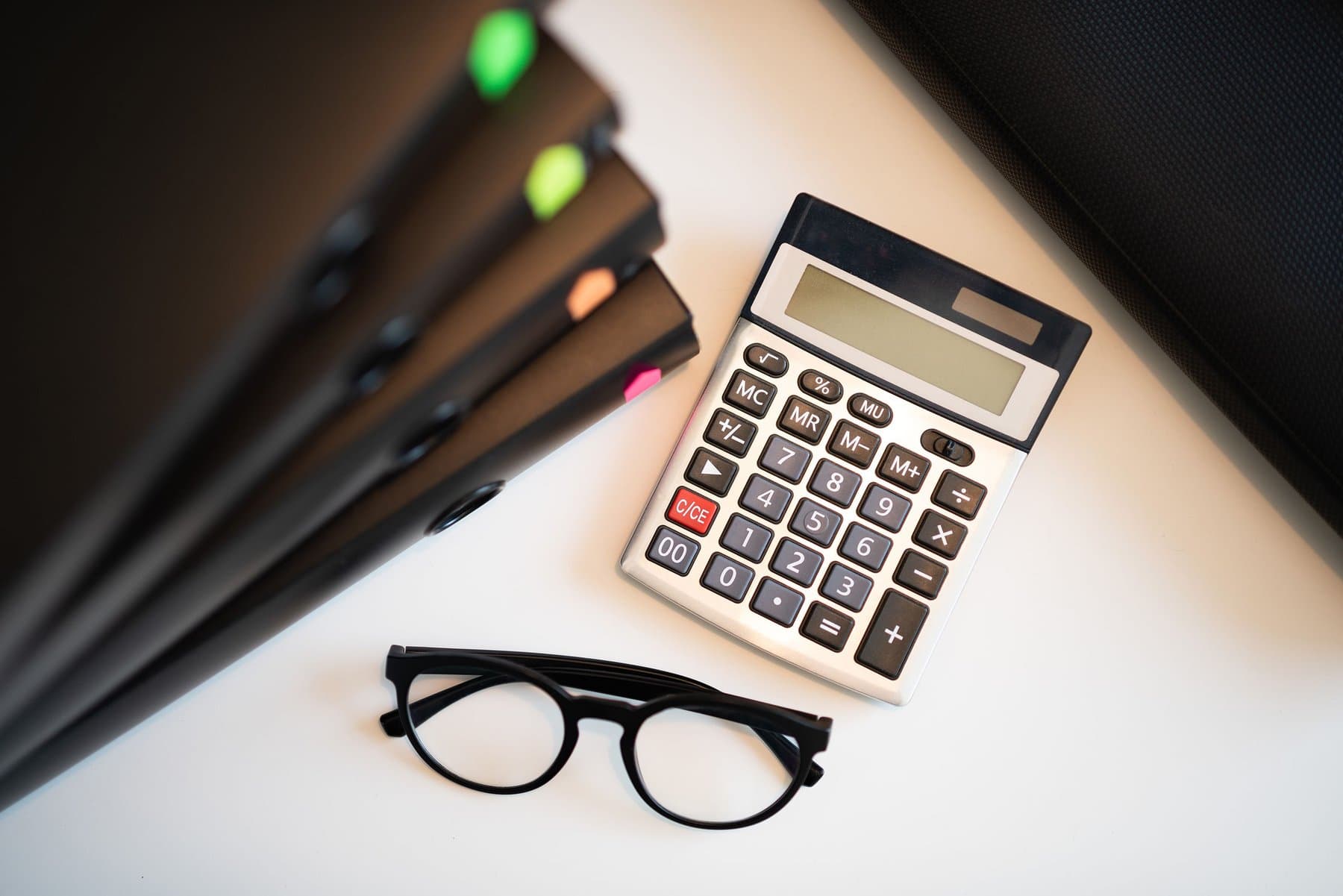 A desk with a calculator, glasses, and loan paperwork in folders