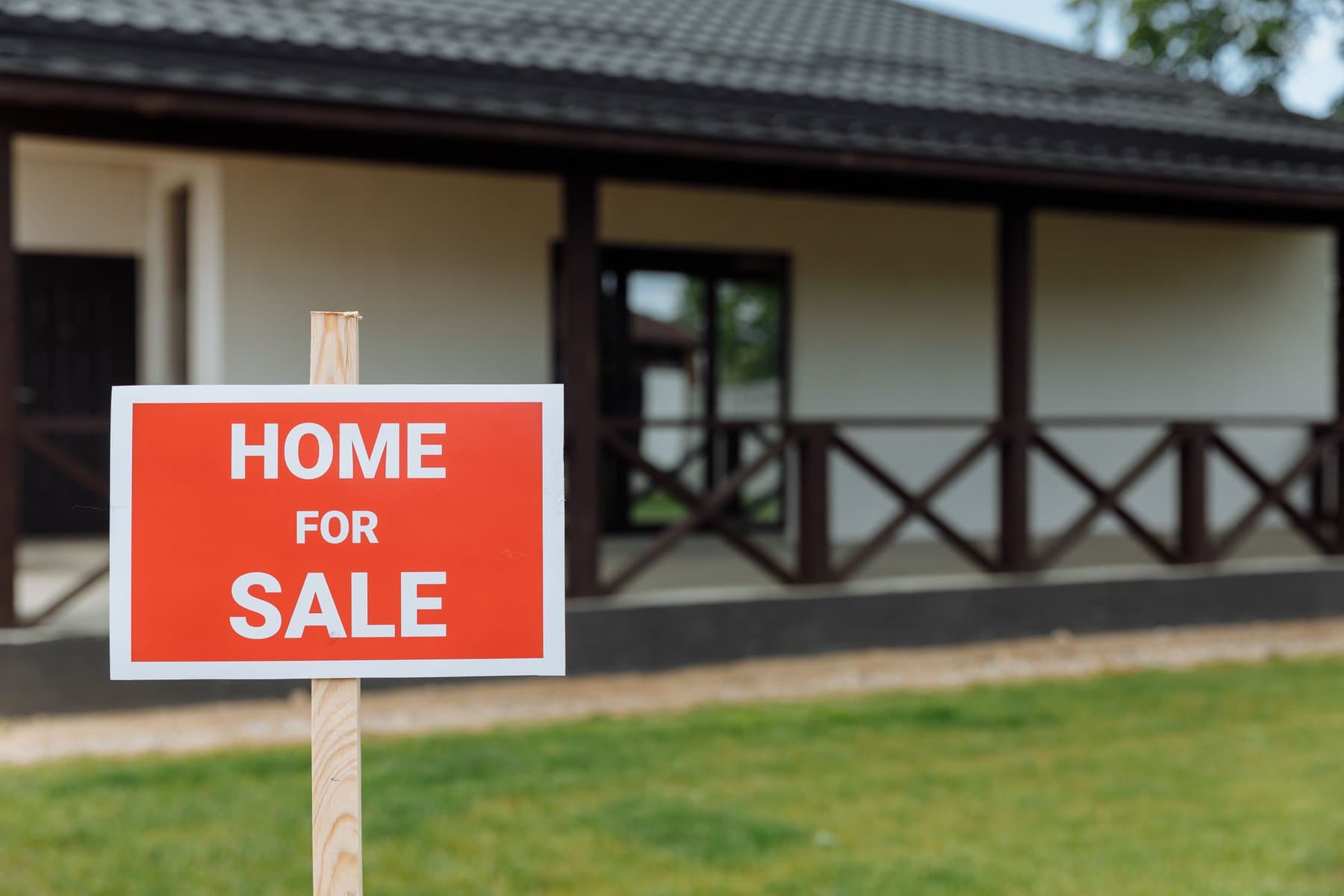 A HOME FOR SALE yard sign in front of a brown-roofed house