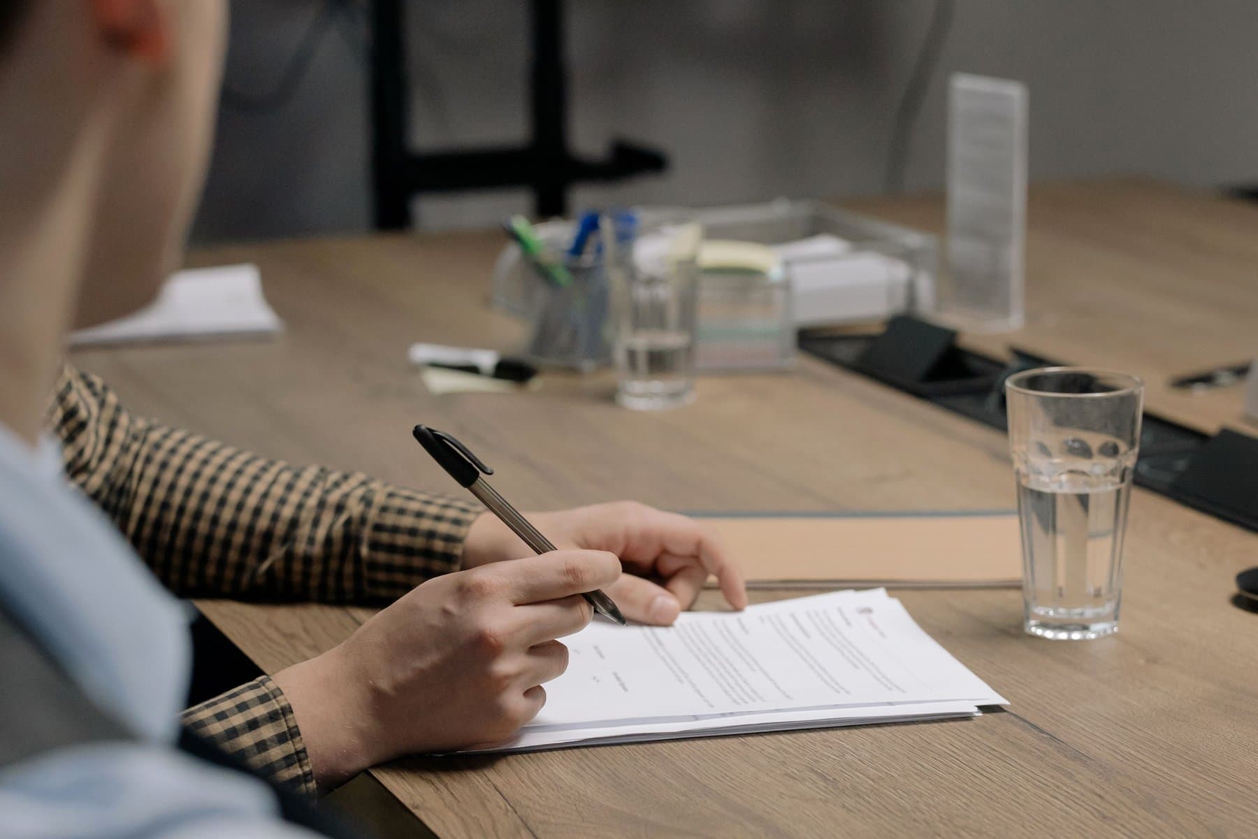 A hand signing a document at a wood conference table